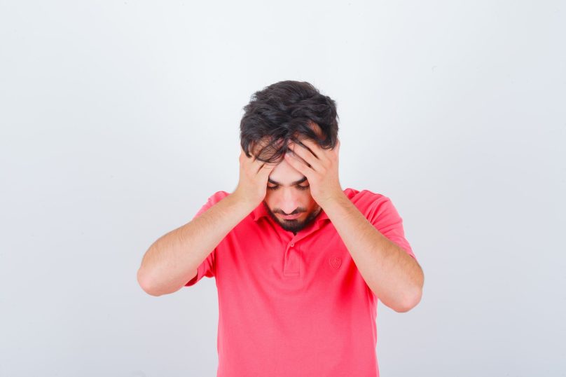 young-male-holding-hands-head-pink-t-shirt-looking-distressed-front-view (1)